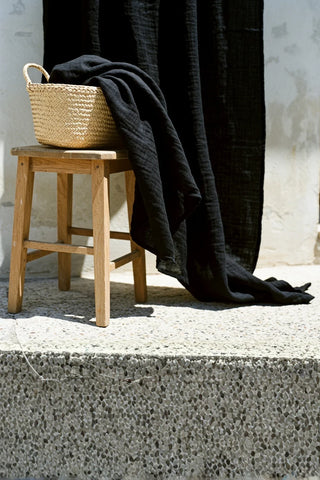 Black fabric draped over basket and wooden stool. Handwoven 2-layer muslin cotton curtain, Denizli, OEKO-TEX. Vivamaison.