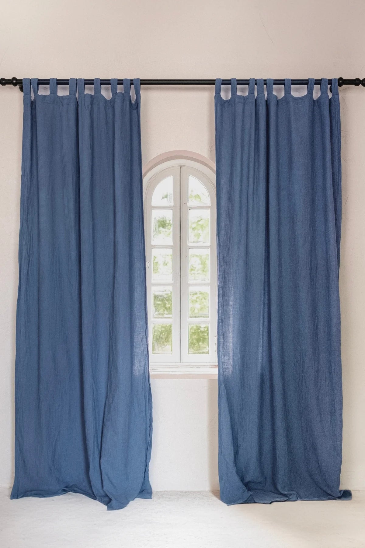 Two blue tab top panels framing arched window. Handwoven 2-layer muslin cotton curtain, Denizli, OEKO-TEX. Vivamaison.