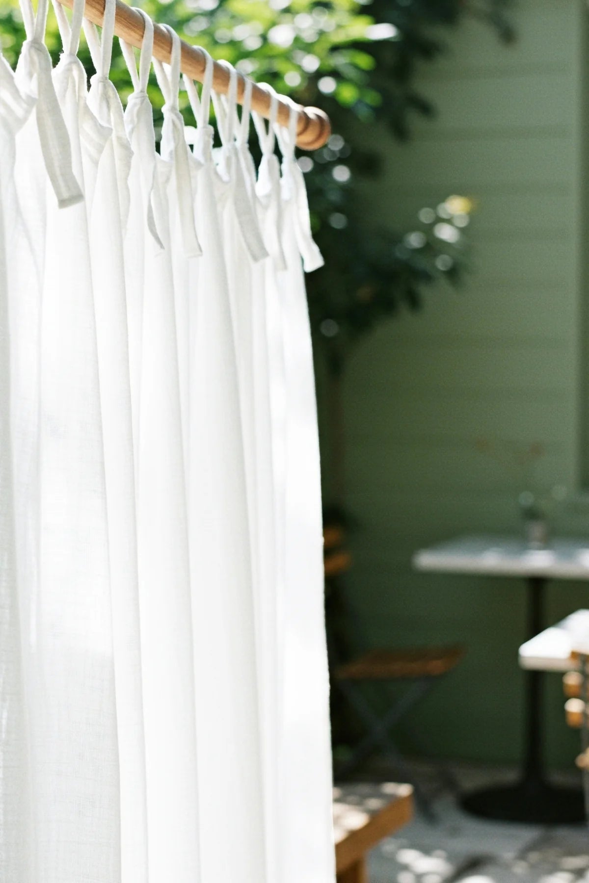 White tie knots closeup on wooden rod, patio. Handwoven 2-layer muslin cotton curtain, Denizli, OEKO-TEX. Vivamaison.