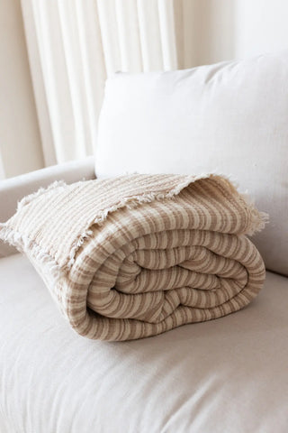 Latte Striped handwoven 8-layer muslin Turkish cotton quilt folded flat lay. Hand-tied fringe Denizli, OEKO-TEX. Vivamaison.