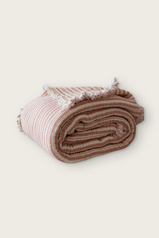 Handwoven 8-layer muslin Turkish cotton quilt in terracotta striped, rolled front view with hand-tied fringe