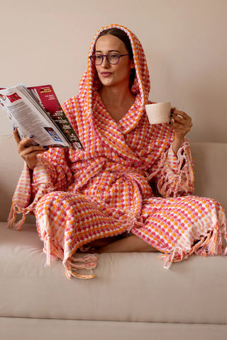 Pink orange chickpea bathrobe hood up seated lifestyle. Handwoven Turkish cotton Denizli, OEKO-TEX. Vivamaison.