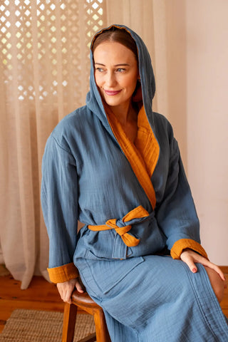 Double-sided muslin bathrobe indigo-mustard hood up seated. Handwoven Turkish cotton Denizli, OEKO-TEX. Vivamaison.