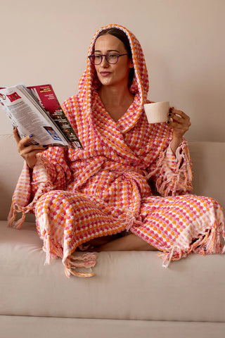 Pink orange mosaic bathrobe hood up seated lifestyle. Handwoven Turkish cotton Denizli, OEKO-TEX. Vivamaison.