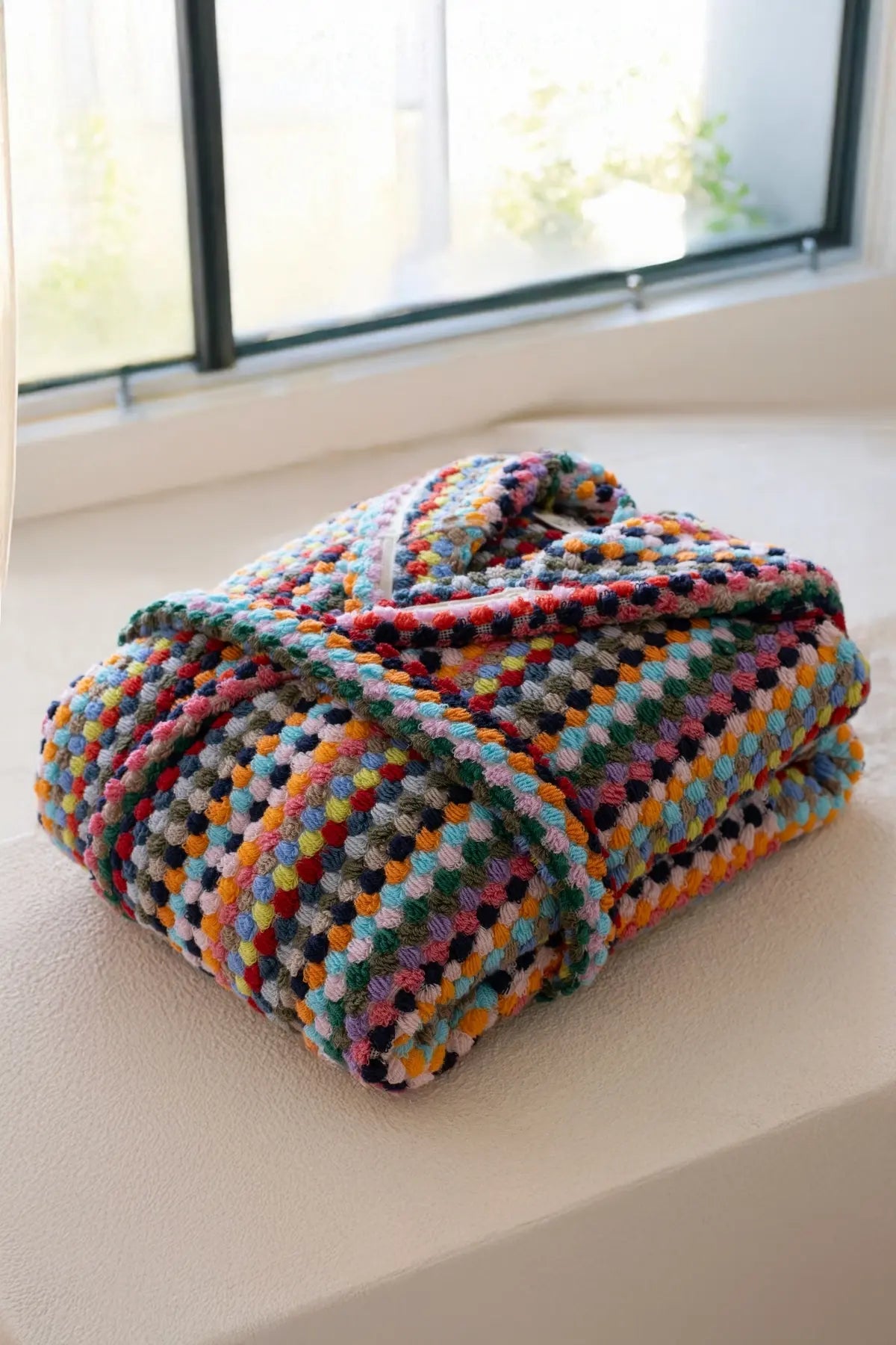 Rainbow mosaic bathrobe folded by window. Handwoven Turkish cotton Denizli, OEKO-TEX. Vivamaison.