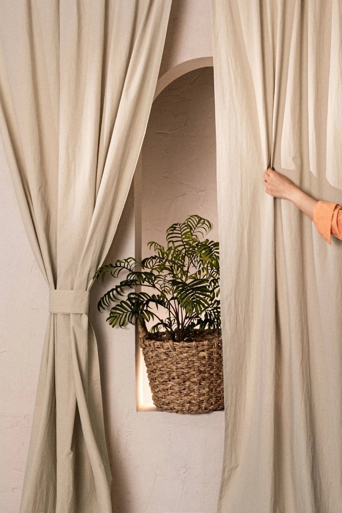 Hand opening a beige stonewashed cotton curtain with tieback. Handwoven in Denizli, OEKO-TEX. Vivamaison.