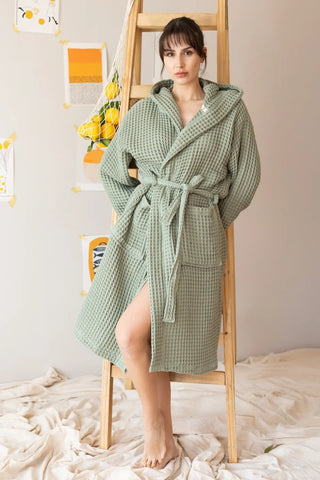 Handwoven waffle hooded bathrobe in sage green, front view on ladder. Turkish cotton from Denizli, OEKO-TEX. Vivamaison.