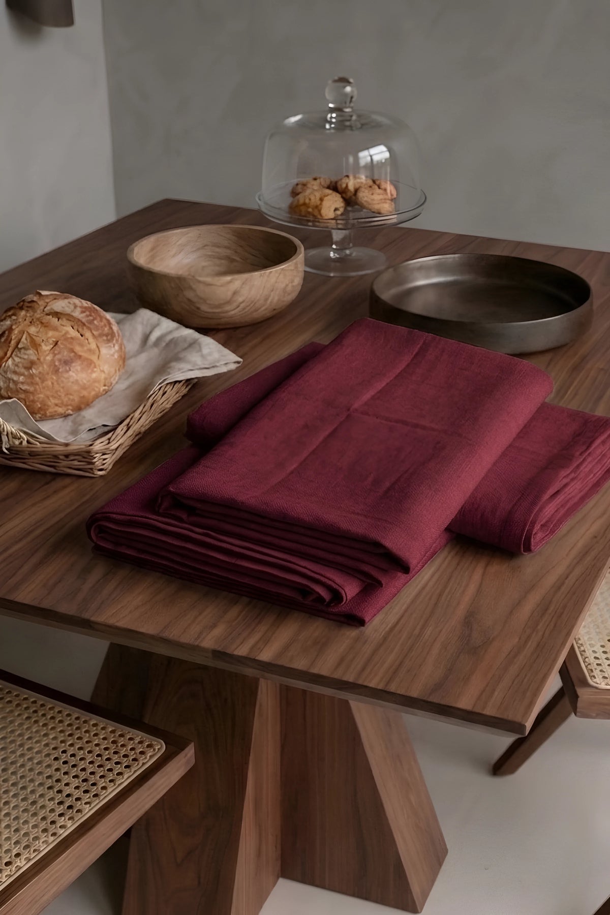 Burgundy plain linen cotton blend tablecloth folded on a walnut dining table beside a bread basket. 9 sizes, handmade in Denizli, OEKO-TEX. VivaMaison.