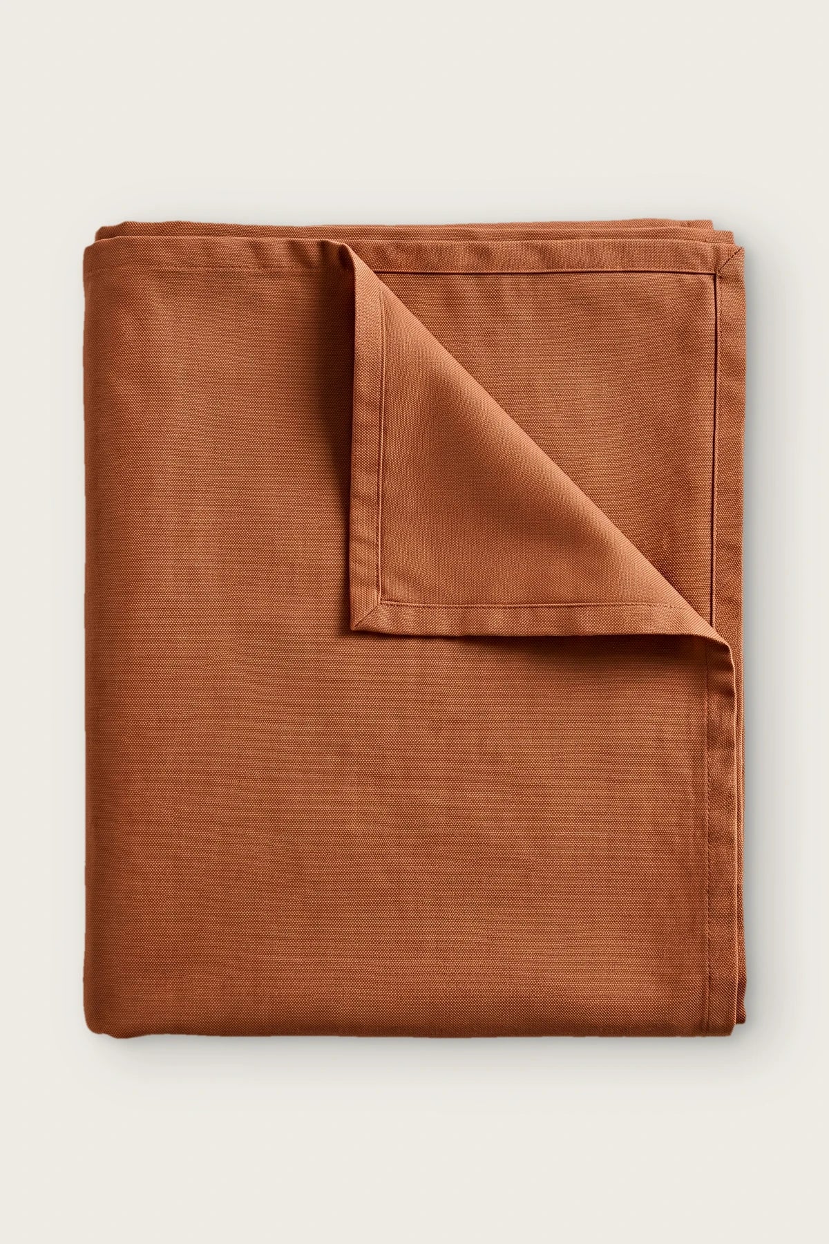Plain linen cotton blend tablecloth in cinnamon, folded with corner turned back