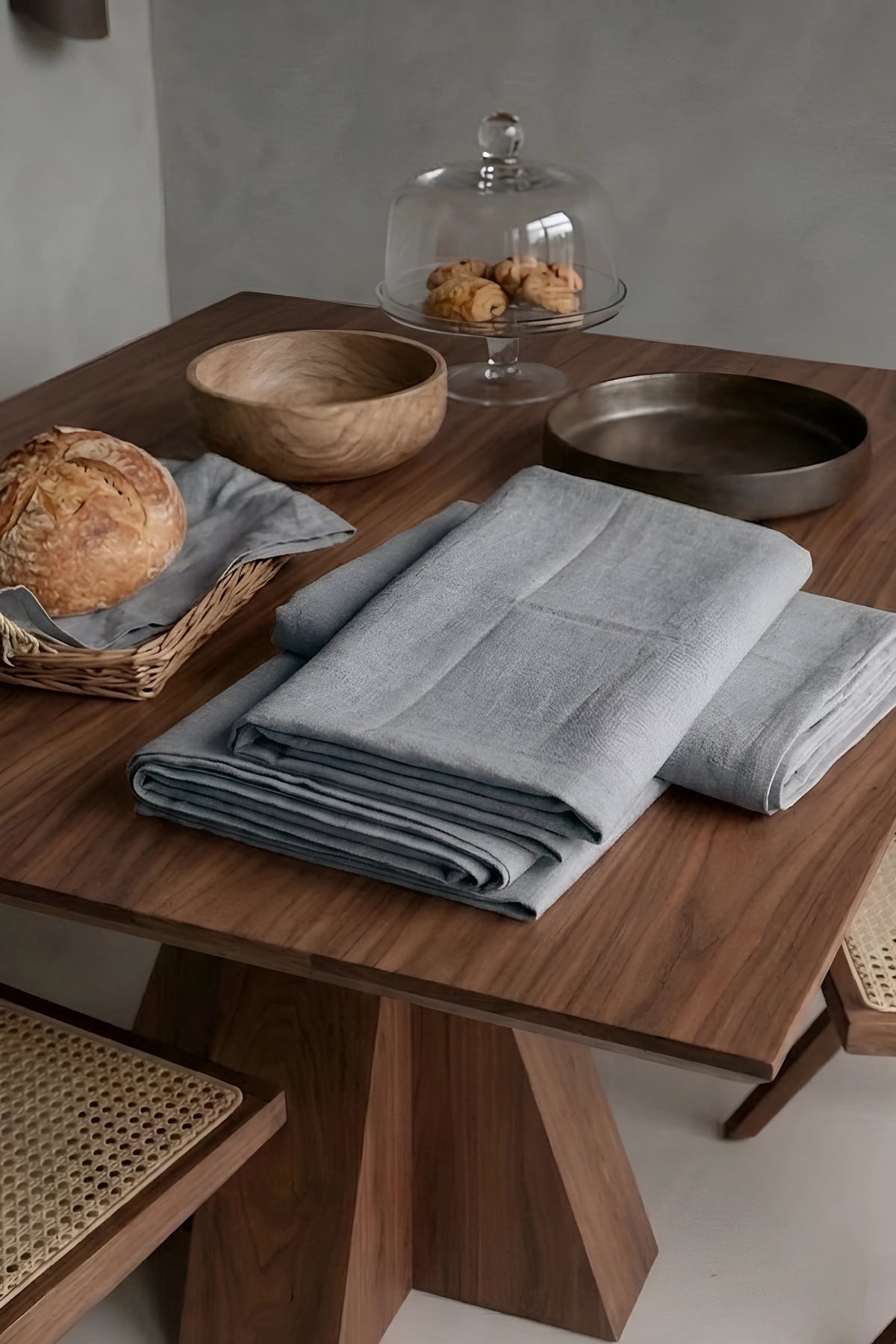 Gray plain linen cotton blend tablecloth folded on a walnut dining table beside a bread basket. 9 sizes, handmade in Denizli, OEKO-TEX. VivaMaison.