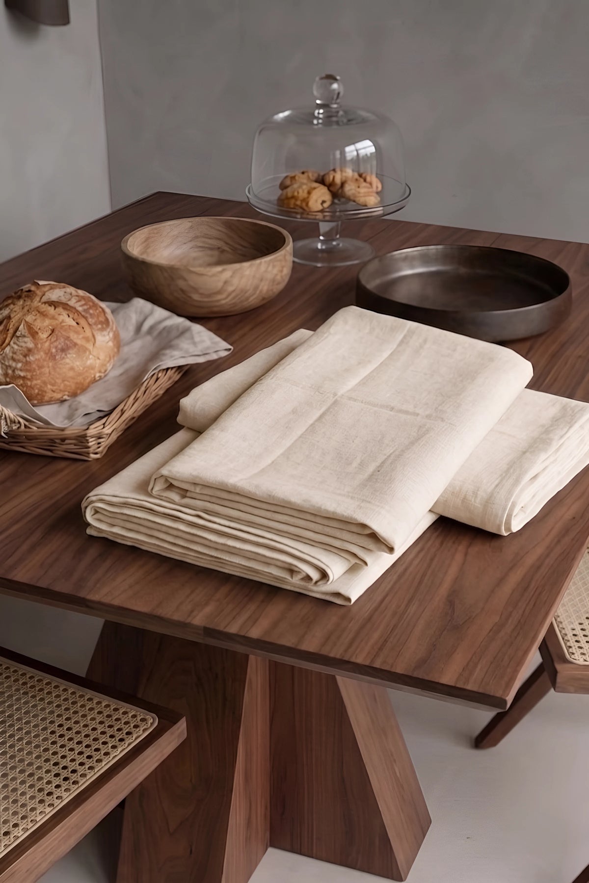 Natural plain linen cotton blend tablecloth folded on a walnut dining table beside a bread basket. 9 sizes, handmade in Denizli, OEKO-TEX. VivaMaison.