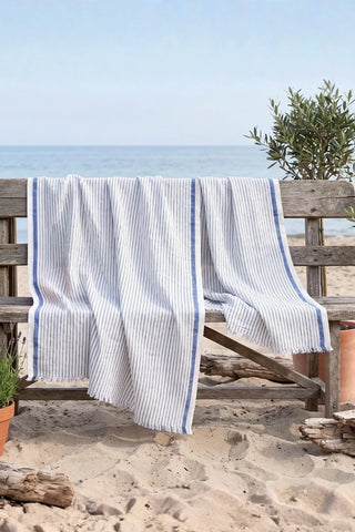 Muslin striped Turkish cotton beach towel peshtemal with blue stripes draped on a beach bench by the sea - VivaMaison