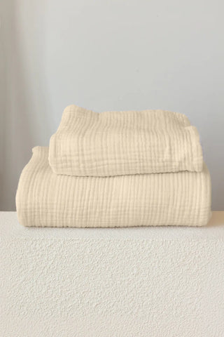 Folded natural-tone handwoven muslin towels detailing the airy 4-layer cotton texture, OEKO-TEX certified