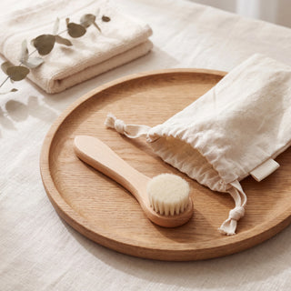 Natural bristle dry face brush with its cotton drawstring pouch on a wooden tray - VivaMaison